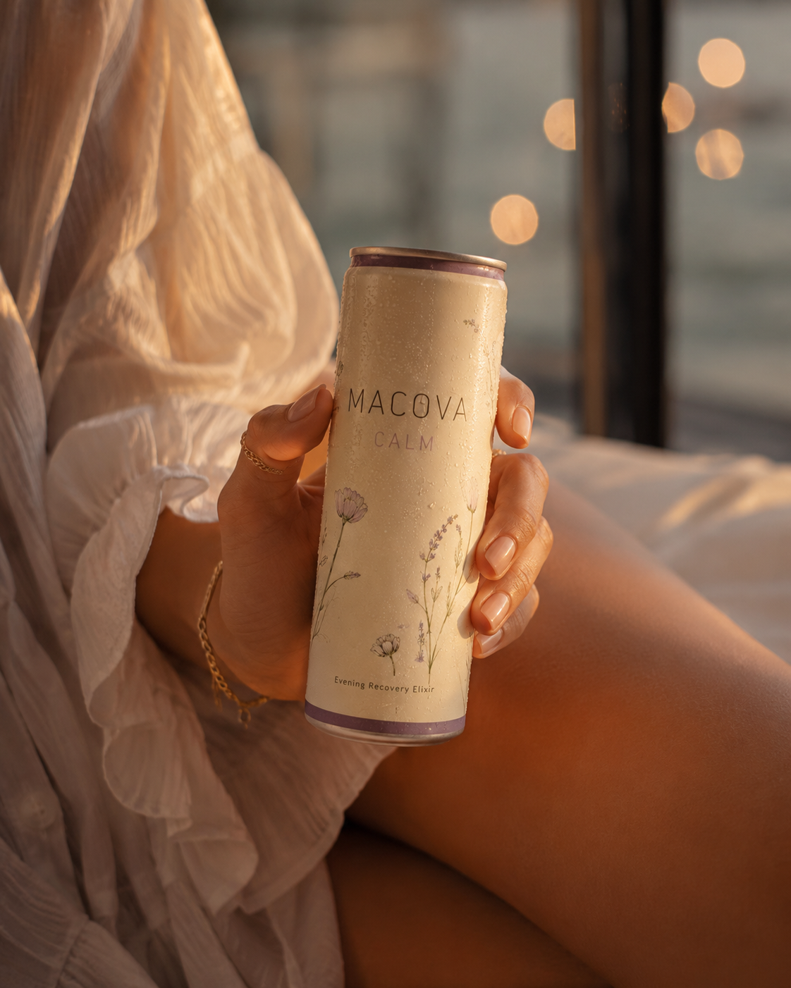 Woman in a cream robe holding a MACOVA can in soft evening light